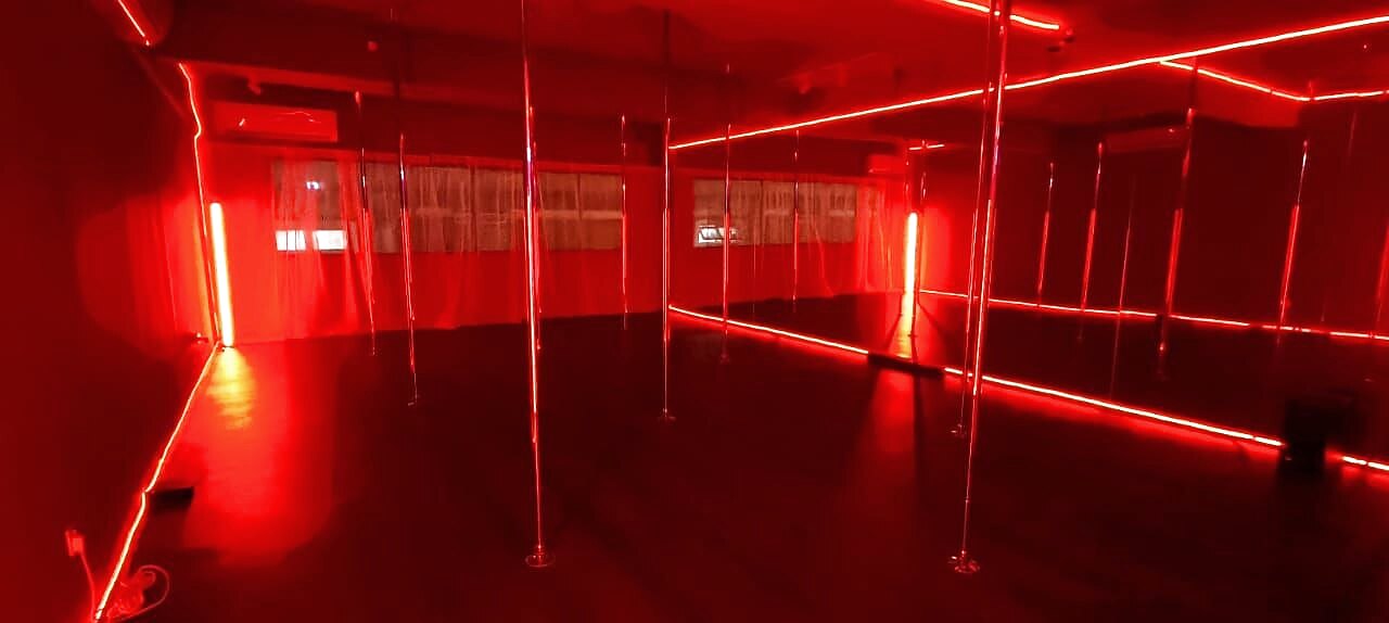 The red-lit Sinner Room at Angels Pole Studio with chrome poles and neon lights
